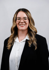 Porträtfoto eines weiblichen Teammitglieds mit gewelltem Haar und Brille.